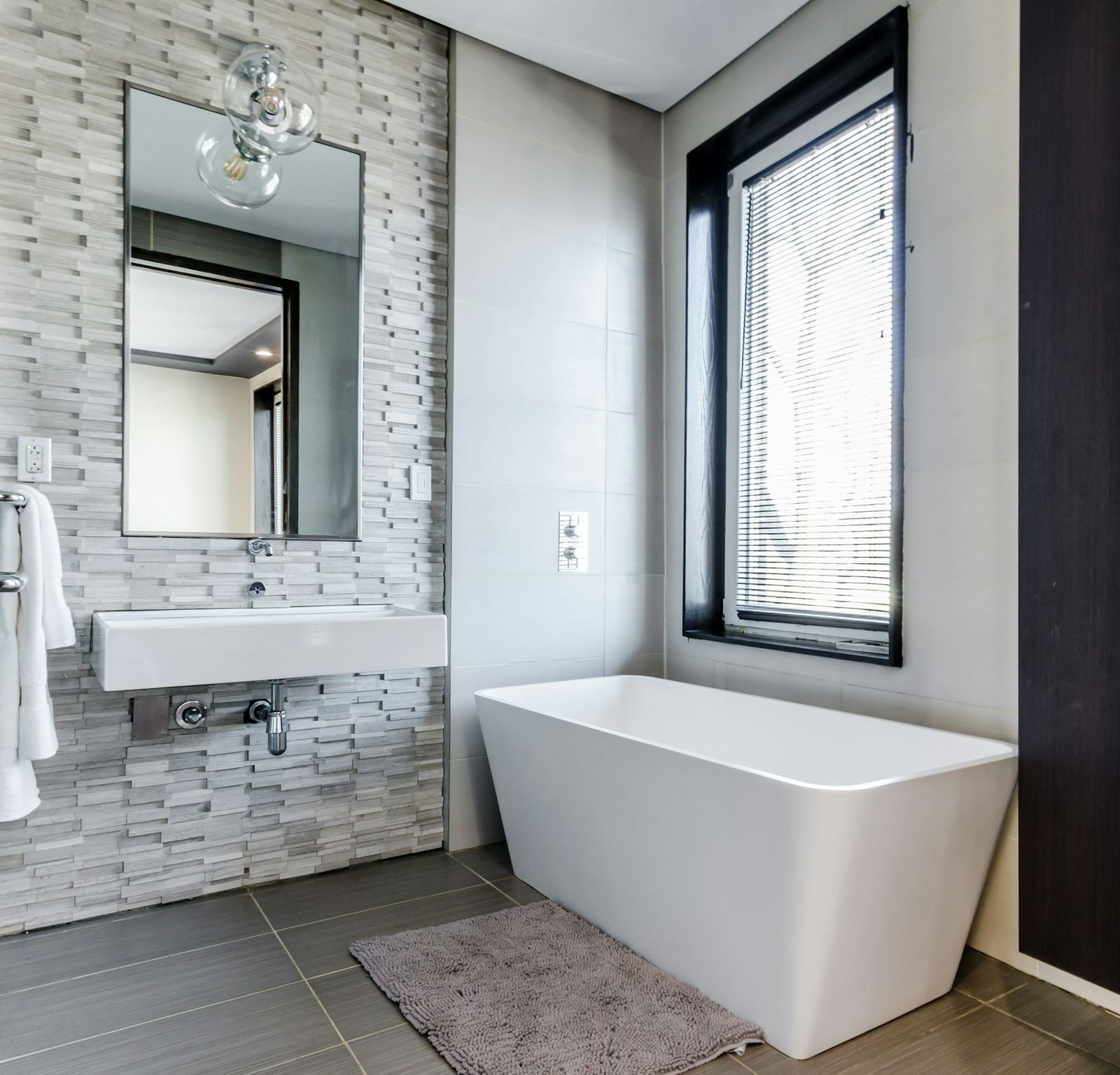 Modern bathroom with a freestanding rectangular tub, stone-tile wall and a tall black-framed window